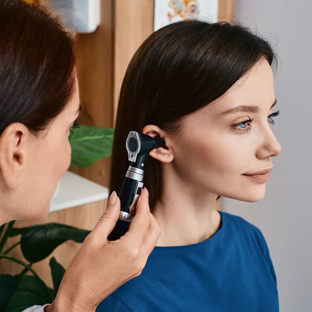 Audiologist with otoscope in female patient's ear