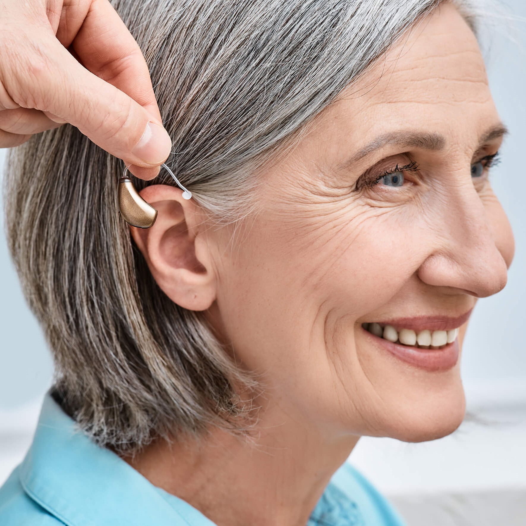 Audiologist holding hearing aid by female patient's ear