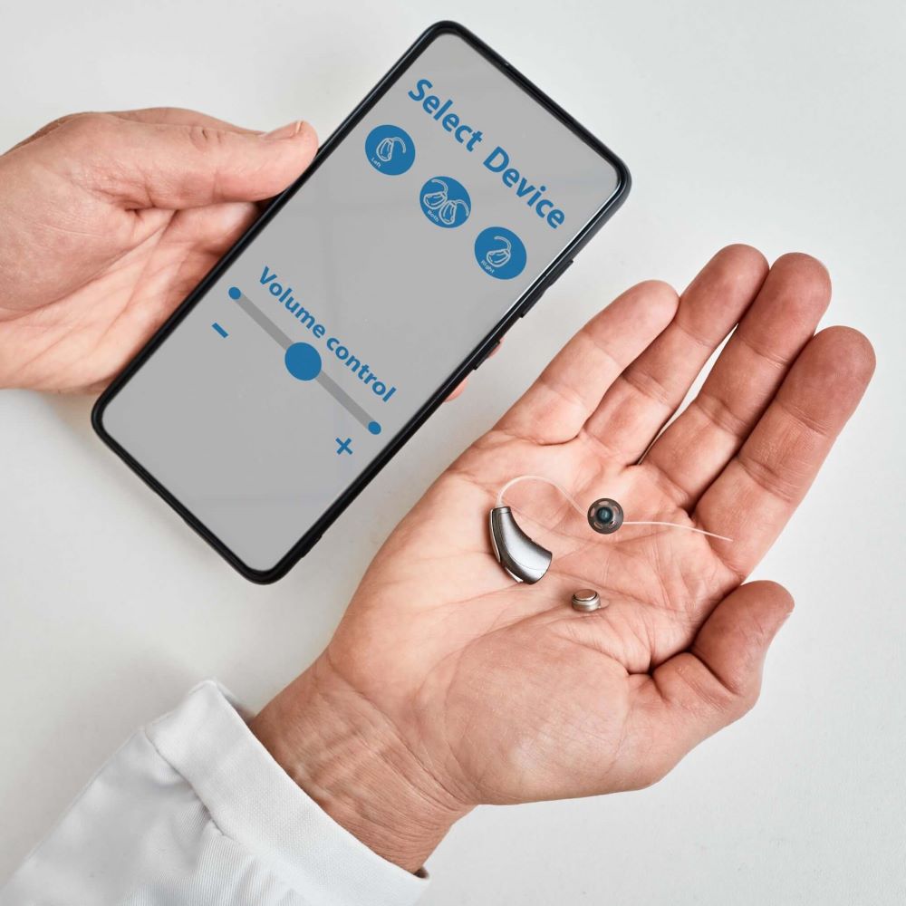 Audiologist holding hearing aid and smart phone with hearing aid app open