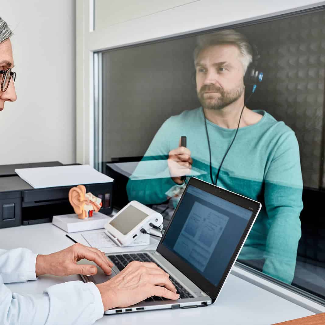 Audiologist giving patient hearing test in hearing booth