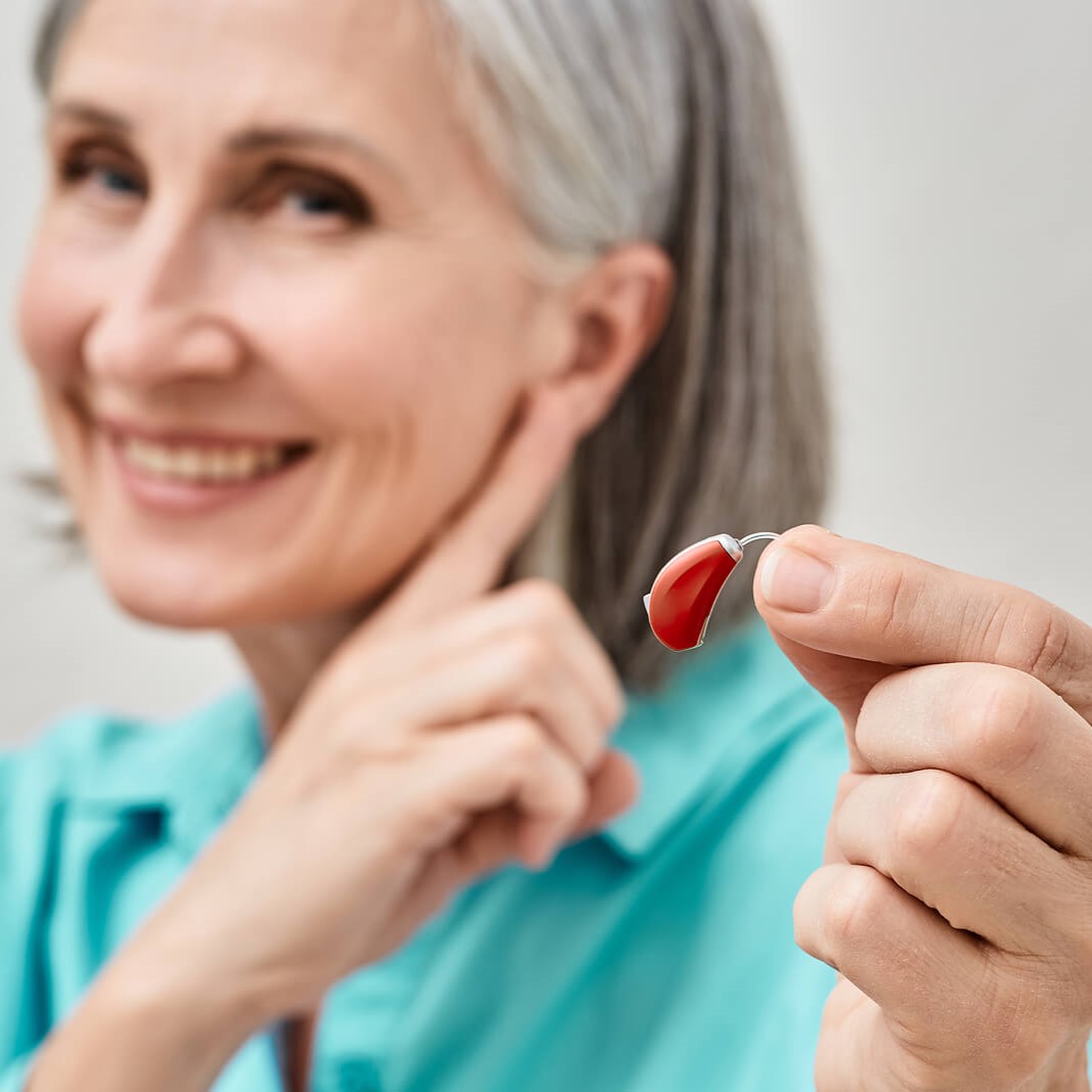 Woman holding a hearing aid and pointing finger at ear