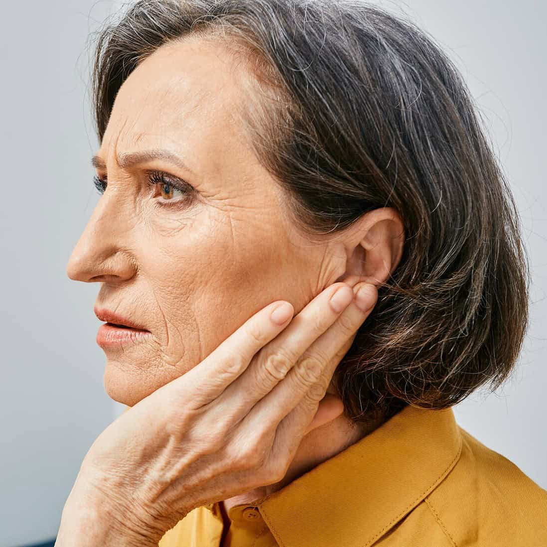 Mature woman holding hand to left ear